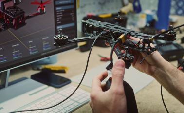 about_us-jiop-sprints Drone held up to monitor with 3D design of drone