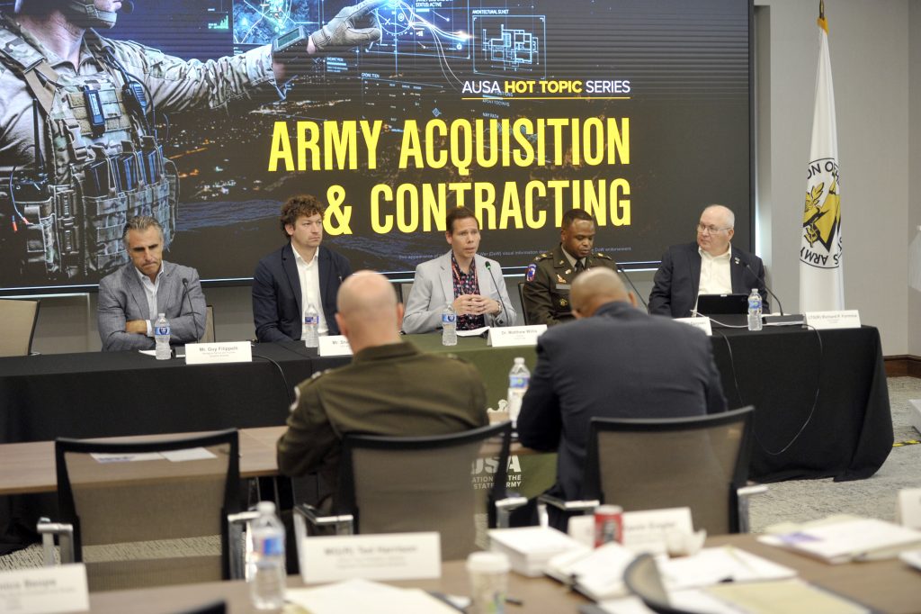 Panel at AUSA Hot Topic Army Acquisition and Contracting with 5 panelists sitting at table in front of an audience.