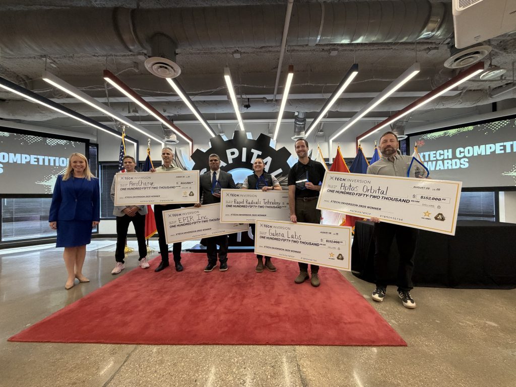 Individuals standing in conference center on red rug with large checks in hand.